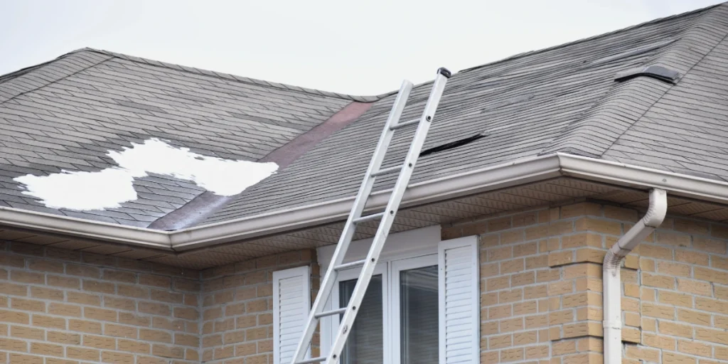 Residential roof with missing and damaged shingles and a ladder leaning against the gutters