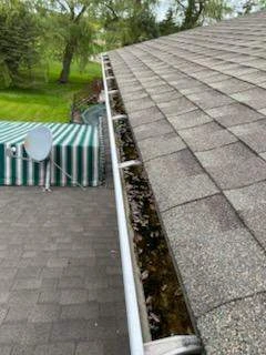 Clogged gutter filled with leaves and debris along an asphalt shingle roof in Angola, NY